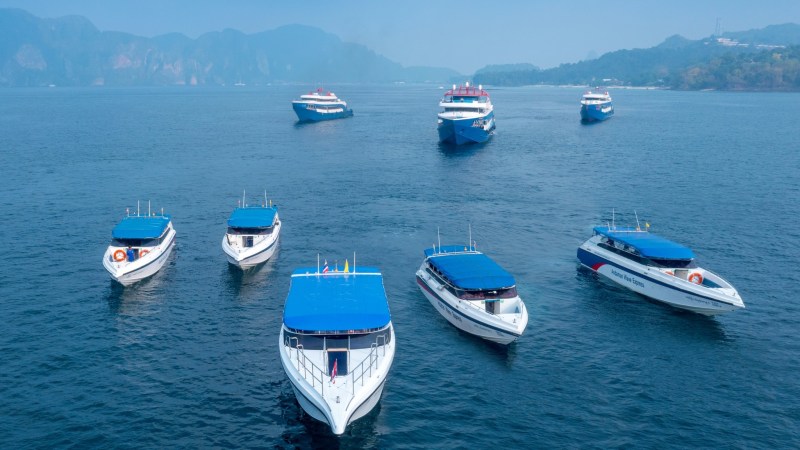 Multiple speedboats with blue canopies on calm water near distant hills.