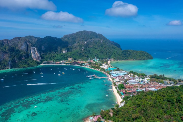Aerial view of a tropical island with turquoise water, boats, and lush greenery.