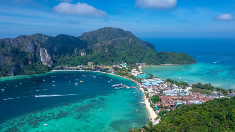 Aerial view of a tropical island with turquoise water, boats, and lush greenery.