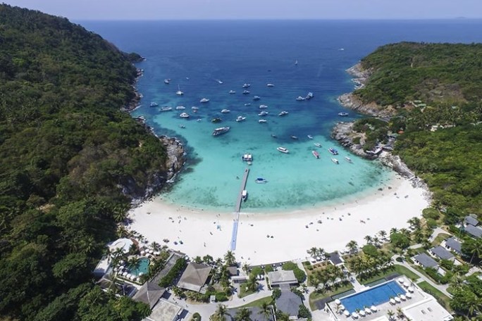 Aerial view of a beach cove with boats and lush greenery.