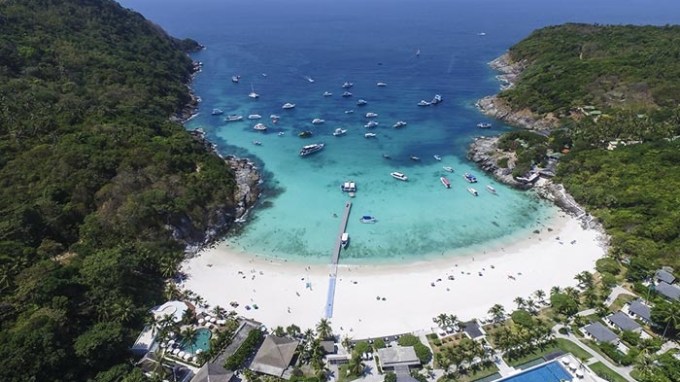 Aerial view of a beach cove with boats and lush greenery.