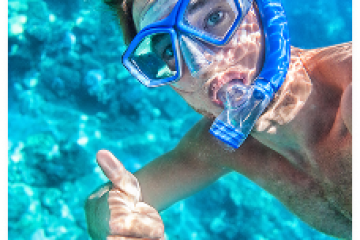 Person snorkeling underwater, wearing a mask and giving a thumbs-up.