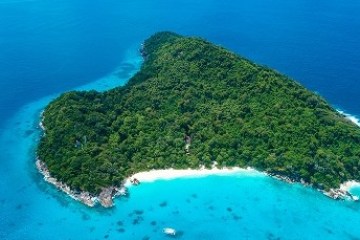Aerial view of a heart-shaped island surrounded by turquoise water and lush greenery.