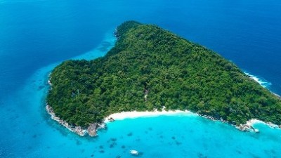 Aerial view of a heart-shaped island surrounded by turquoise water and lush greenery.