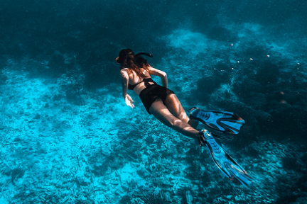 Person snorkeling underwater with fins over coral reef.