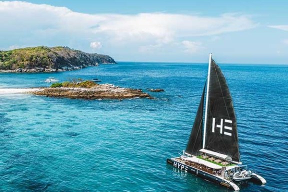 Catamaran sailing near a small island in clear blue sea under a sunny sky.