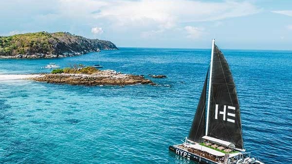 Catamaran sailing near a small island in clear blue sea under a sunny sky.