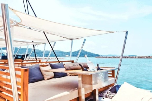 Daybed with pillows on a luxurious yacht deck against a scenic ocean backdrop.