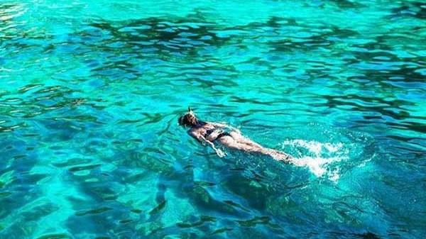 Person snorkeling in clear turquoise water near a rocky shore.
