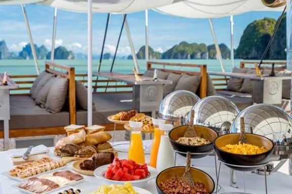 Buffet on a yacht deck with assorted foods, juice, and sea view.