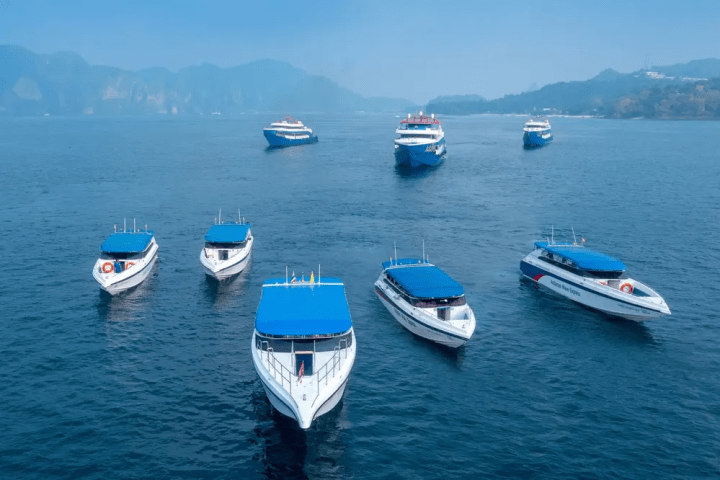 Seven blue-roofed boats on a calm sea with hazy mountains in the background.