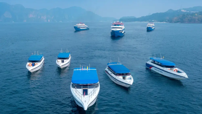 Seven blue-roofed boats on a calm sea with hazy mountains in the background.